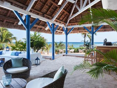 Offener Strandpavillon mit komfortablen Sitzgelegenheiten und Blick auf das blaue Meer.