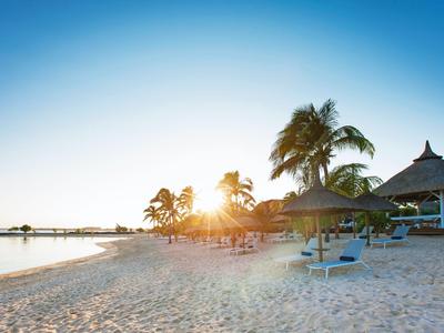 Strand mit Palmen, Sonnenschirmen und Sonnenliegen bei Sonnenuntergang in Urlaubsort.