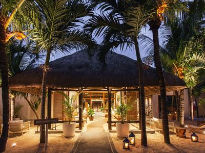 Beleuchteter Eingang eines tropischen Hotels mit Palmen und Holzstruktur bei Nacht.