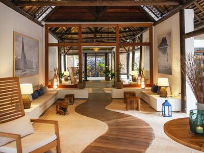 Moderner, heller Hotel-Lounge-Bereich mit Holz- und Sandboden, großen Holzträgern und bequemen Sitzmöbeln.
