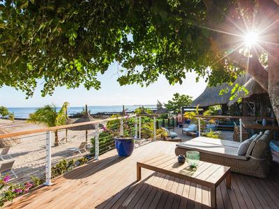 Gemütliche Terrasse mit Sofa und Tisch unter einem Baum mit Blick auf den Strand und das Meer.