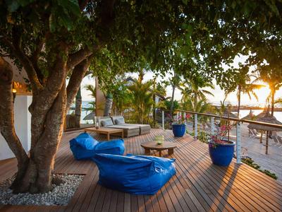 Holzterrasse mit Sitzkissen, Lounge-Möbeln und Meerblick bei Sonnenuntergang.