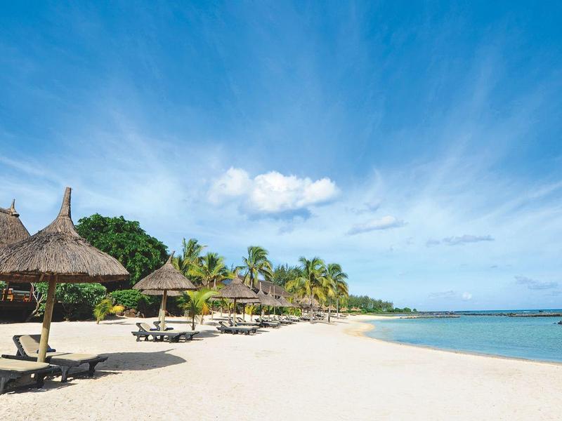 Plage de sable blanc avec des huttes en chaume et des chaises longues sous un ciel bleu au bord de la mer