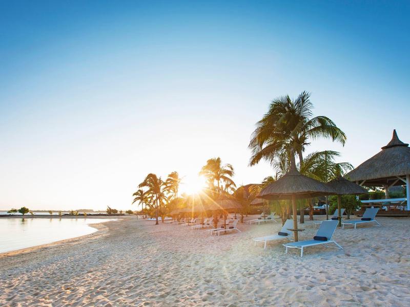 Plage avec palmiers et parasols au coucher du soleil dans une station balnéaire.