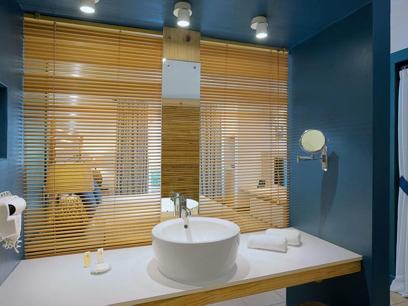 Salle de bain moderne avec lavabo rond, stores en bois et murs bleus.