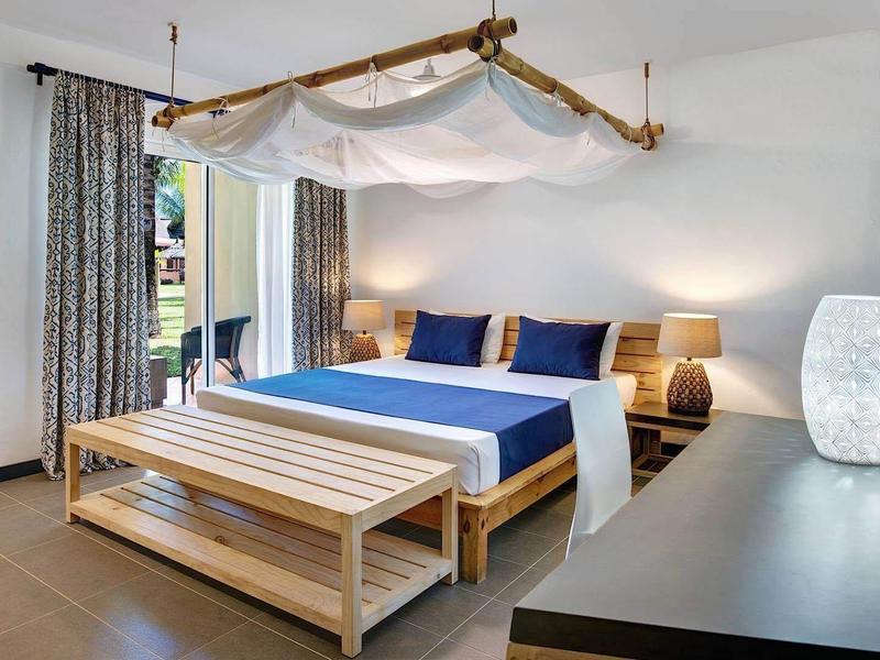 Chambre d'hôtel moderne avec grand lit, banc en bois, lampe et rideaux à la fenêtre.