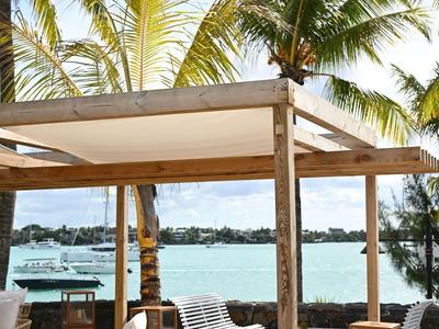 Outdoor-Lounge mit Holzpergola, Stühlen und Blick auf Wasser und Palmen