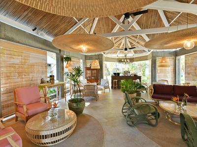 Innenraum einer Hotel-Lounge mit Korbmöbeln, Pflanzen und Decke mit Holzträgern.