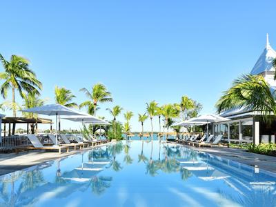 Infinity-Pool mit weißen Sonnenschirmen und Liegestühlen umgeben von Palmen unter klarem blauem Himmel