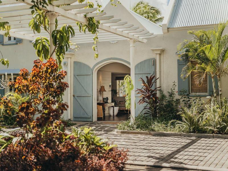 Eingang eines Ferienhauses mit offener Holztür und tropischen Pflanzen im Vordergrund.