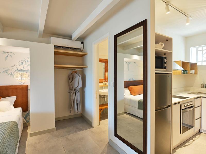 Moderner Hotelzimmerbereich mit offener Garderobe, großem Spiegel und kompakter Küchenzeile.