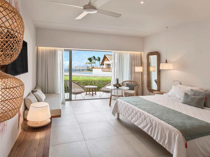 Modernes Hotelzimmer mit großem Bett, Sitzbereich, Deckenventilator und Terrassentür zum Garten.