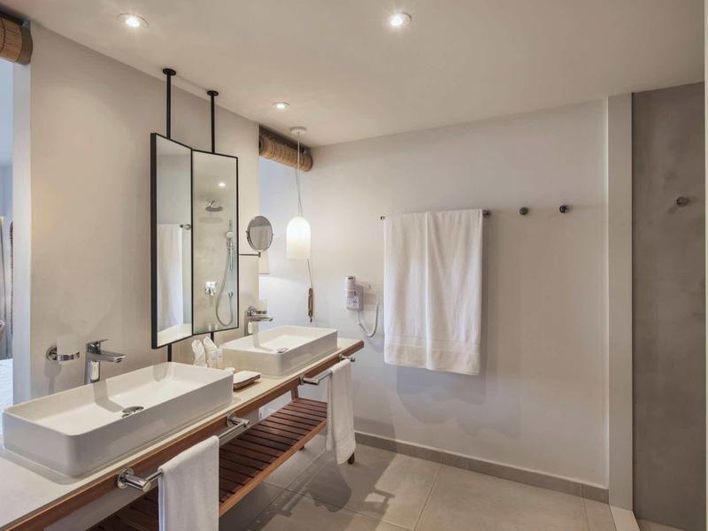 Moderner hellgrauer Badezimmerbereich mit Doppelwaschbecken, großem Spiegel und weißen Handtüchern.