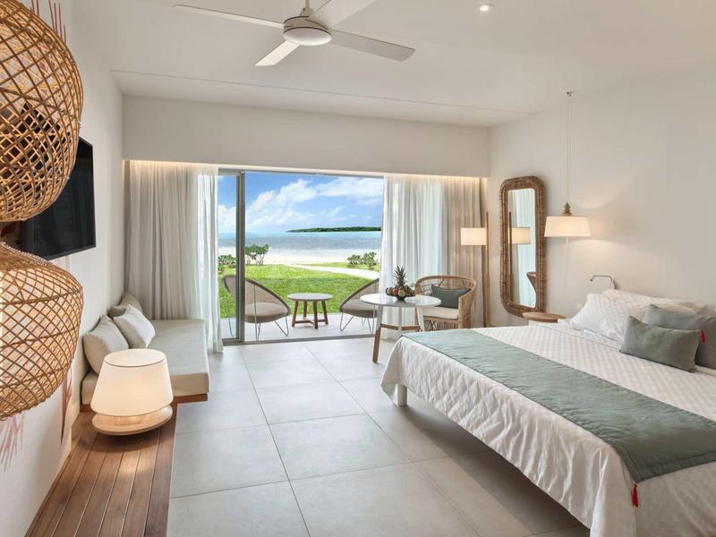 Helles Schlafzimmer mit großem Bett, Terrassentür, Meerblick und modernen Holzmöbeln.