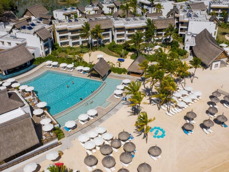Ferienanlage mit Pool, Palmen und Sonnenschirmen am Sandstrand neben dem Meer.