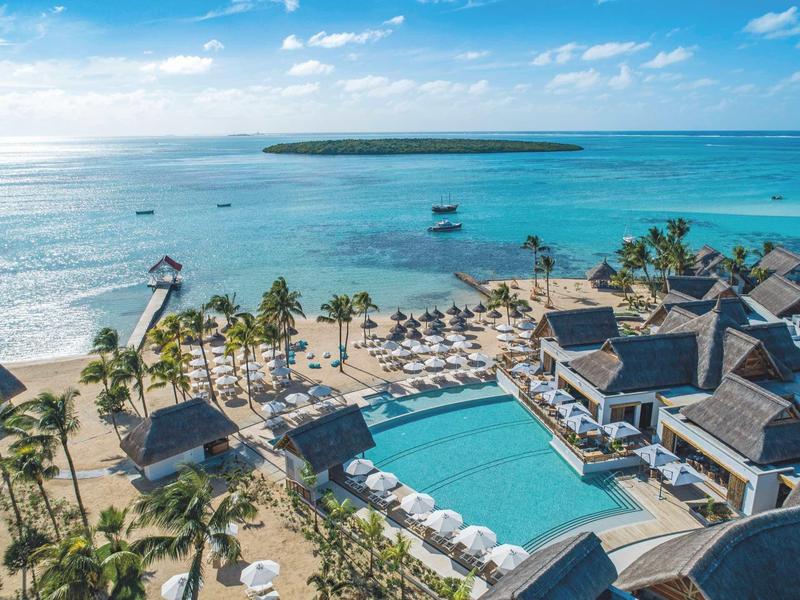Blick auf tropisches Resort mit Pool, Palmen, Strand und blauem Meer unter blauem Himmel.