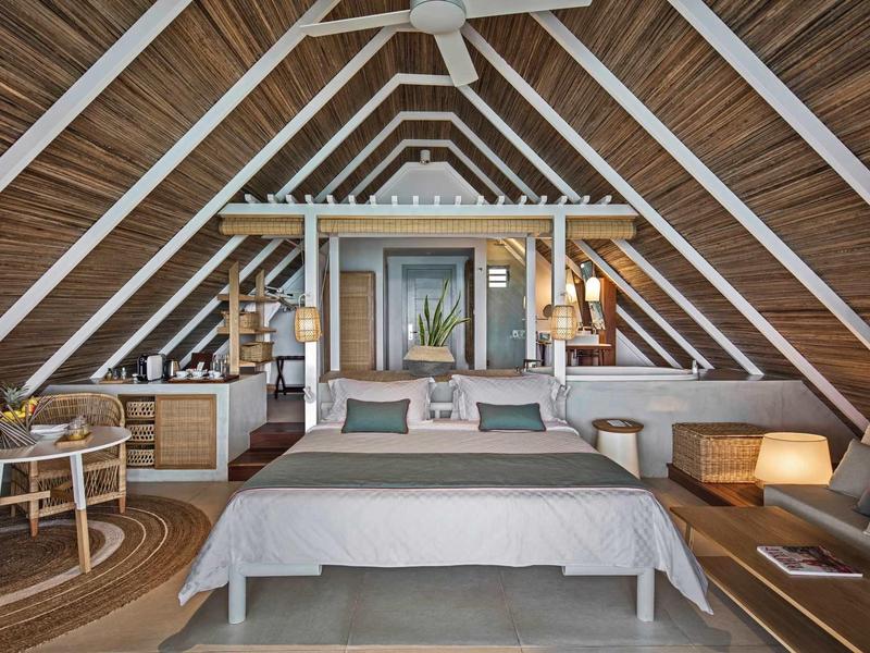 Gemütliches Schlafzimmer unter Dach mit Holzvertäfelung, Doppelbett, Sitzbereich und warmem Licht.