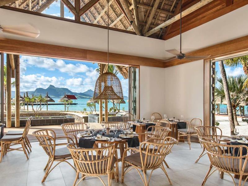 Modernes Café mit runden Holztischen und Stühlen, offener Raum mit Blick auf Meer und Berge.