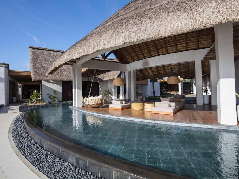 Moderner offener Wohnbereich mit Strohdach und angrenzendem Pool in hellem, mediterranem Stil.