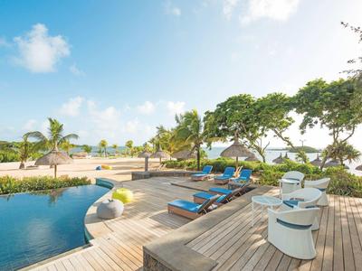 Einladender Poolbereich mit Holzterrasse, Liegestühlen, Stühlen und grünen Bäumen im Hintergrund.