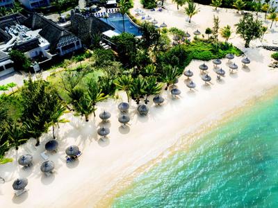 Vista aerea di una spiaggia tropicale con ombrelloni, acqua turchese e vegetazione verde.