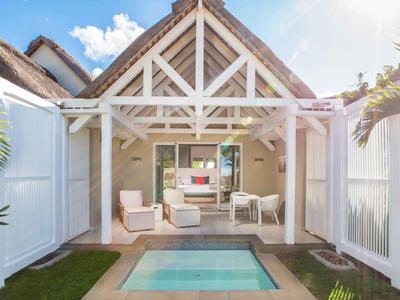 Casa vacacional moderna con pequeña piscina, terraza abierta y detalles de madera blanca bajo cielo azul.