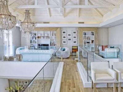 Área de descanso moderna y luminosa con muebles blancos, suelo de madera y estanterías en la pared