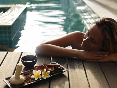 Mujer relajada al borde de la piscina con elementos de spa en tabla de madera, día soleado.