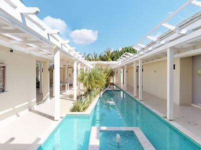 Piscina moderna de hotel con pérgola y paredes blancas, cielo soleado y vegetación al fondo.
