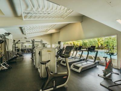 Gimnasio luminoso con equipos modernos y grandes ventanas con vista a la piscina.