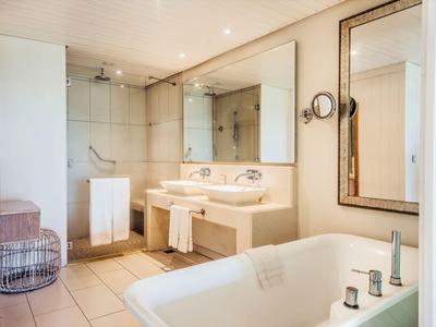 Baño moderno de hotel con bañera, lavabo doble y ducha a ras de suelo.