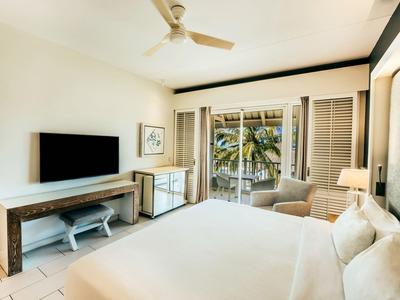 Habitación de hotel luminosa con cama grande, televisor, escritorio y balcón con vista a palmeras.