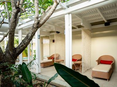 Patio con sillas lounge y sombra de un árbol en una zona del hotel.