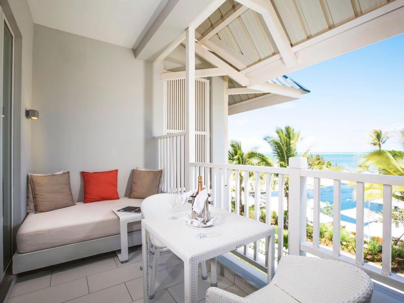 Balcón acogedor con sofá y mesa con vista al mar y palmeras de fondo.