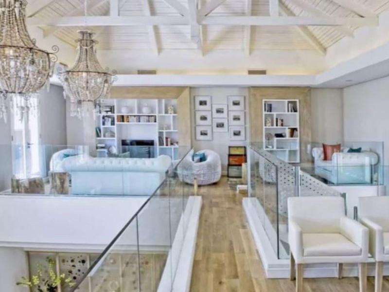 Área de descanso moderna y luminosa con muebles blancos, suelo de madera y estanterías en la pared