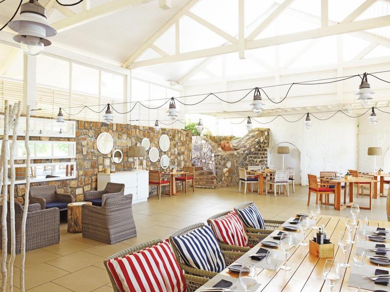Restaurante moderno y luminoso con mesas de madera, sillas acolchadas y pared decorativa de piedra.
