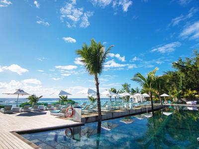 Area piscina di lusso con ombrelloni e palme di fronte al mare sotto un cielo blu.