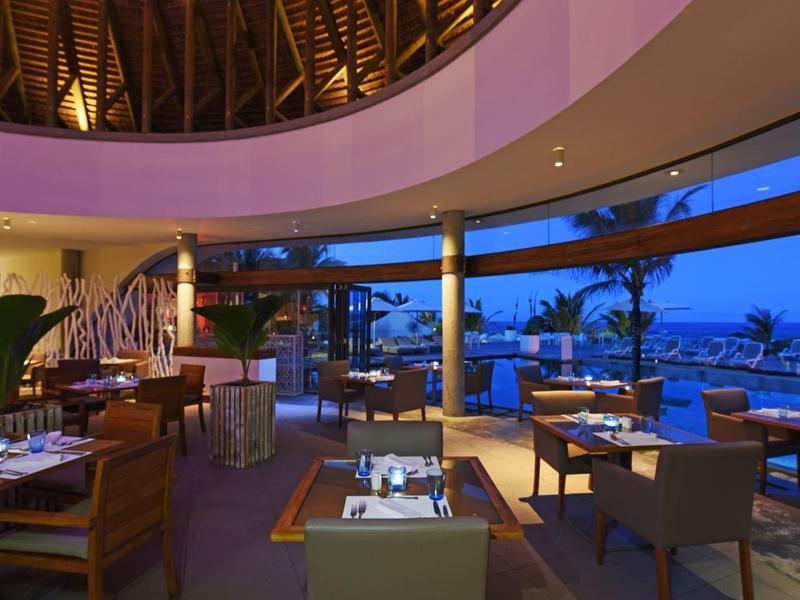 Modern restaurant with wooden furniture and panoramic sea view at dusk.
