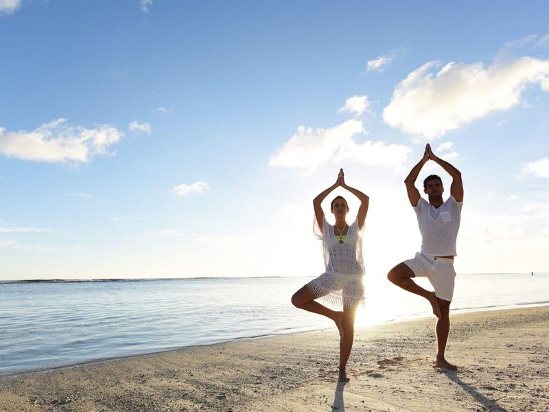 Two people practicing yoga on a calm beach under clear sky and sunny weather.