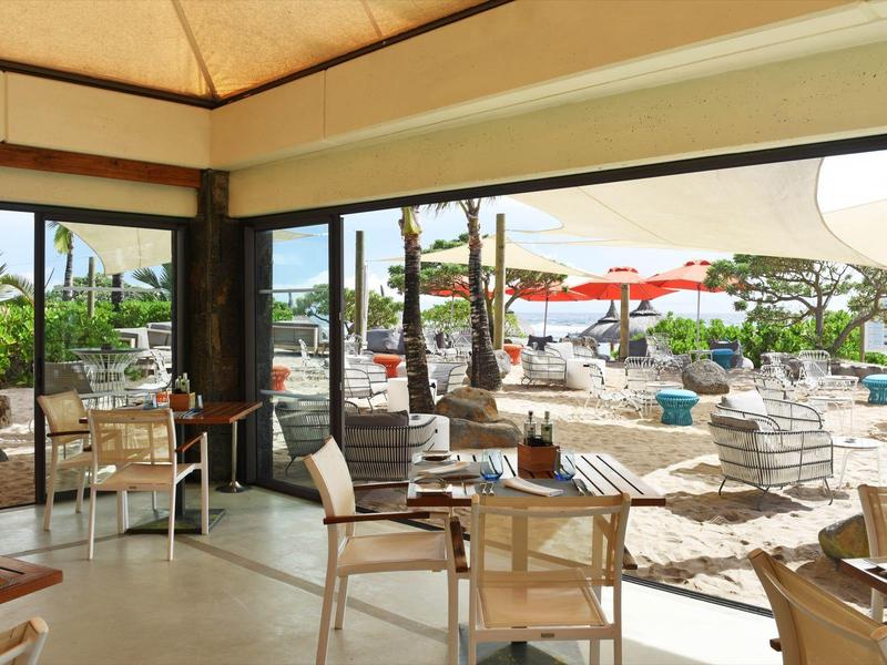 View from a covered seating area overlooking a pool with loungers and umbrellas at a hotel.