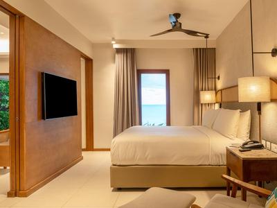 Modern eingerichtetes Schlafzimmer mit großem Bett, Deckenventilator und Blick auf Meer.