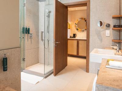 Modernes Badezimmer mit Dusche, Waschbecken, Holztür und angrenzendem Bereich mit rundem Spiegel.