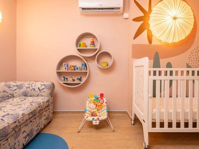 Kindergartenzimmer mit Babybett, blauem Teppich, runden Wandregalen und beigem Sofa.