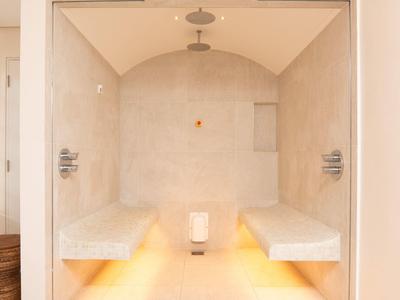 Moderner Dampfraum mit hellbeigen Wänden, zwei Sitzbänken und indirekter Beleuchtung am Boden.