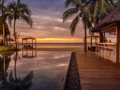 Pool und Bar am Strand mit Palmen bei Sonnenuntergang, ruhig und farbenfroh.