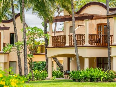 Ein helles Haus mit braunen Balkonen, umgeben von Palmen und grünem Rasen.