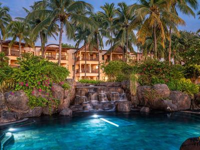 Hotel z oświetlonym basenem, wodospadem i palmami o zachodzie słońca