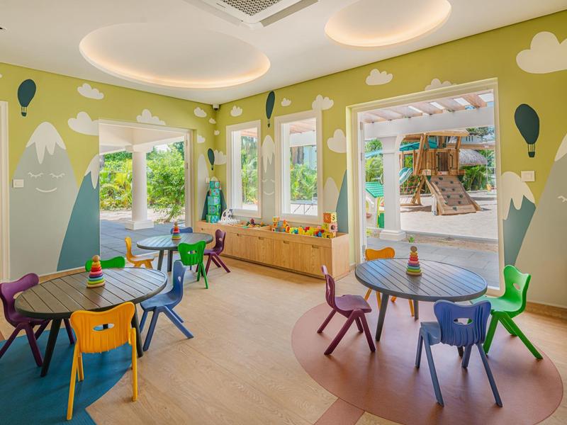 Buntes Kinderzimmer mit kleinen Tischen, bunten Stühlen und Wänden mit Berg- und Ballonmotiven.