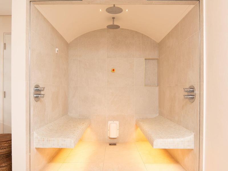 Moderner Dampfraum mit hellbeigen Wänden, zwei Sitzbänken und indirekter Beleuchtung am Boden.