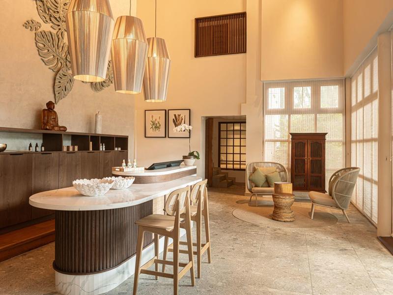 Hell eingerichteter Raum mit Bar, Hockern, großen Fenstern und stilvollen Sitzmöbeln.